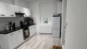 A modern kitchen with white cabinetry, a black countertop, and a wooden floor. - Spacious 2-Bed Doncaster | Ideal for Teams (South Yorkshire)