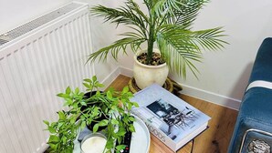 A corner of a room with a radiator, a potted plant, a remote control, a glass of milk, and a magazine on a small table. - Spacious 2-Bed Doncaster | Ideal for Teams (South Yorkshire)