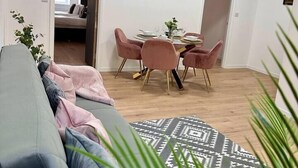 A modern living room with a grey sofa, pink chairs, a dining table, and a TV mounted on the wall. - Spacious 2-Bed Doncaster | Ideal for Teams (South Yorkshire)