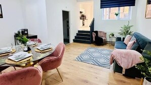 A spacious living area with a dining table set for four, a sofa, and a staircase leading to an upper level. - Spacious 2-Bed Doncaster | Ideal for Teams (South Yorkshire)