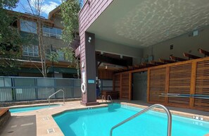 Piscina ao ar livre com deck de madeira, posto de salva-vidas e área de estar coberta.