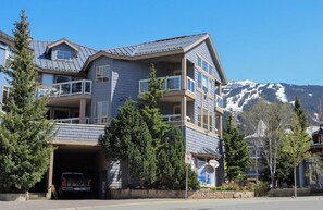 A multi-story building with a garage entrance, balconies, and a mountain backdrop. - Central Village Mountain Retreat w/ Kitchen | Pool & Hot Tub (Whistler)