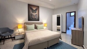 Ein Schlafzimmer mit einem Bett, Nachttischlampen, einem Sessel, einem Kleiderschrank und einem Wandbild mit Schmetterlingen.