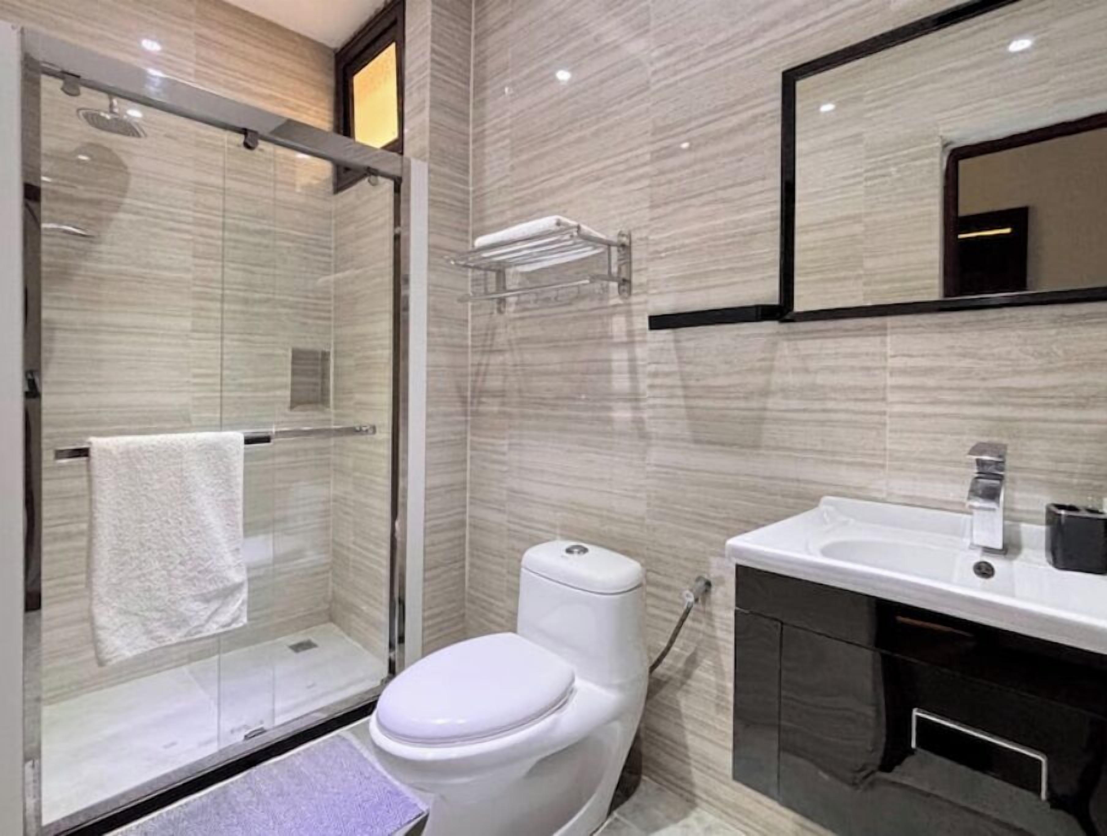 A modern bathroom with a glass shower enclosure, a white toilet, and a sink with a mirror above it.
