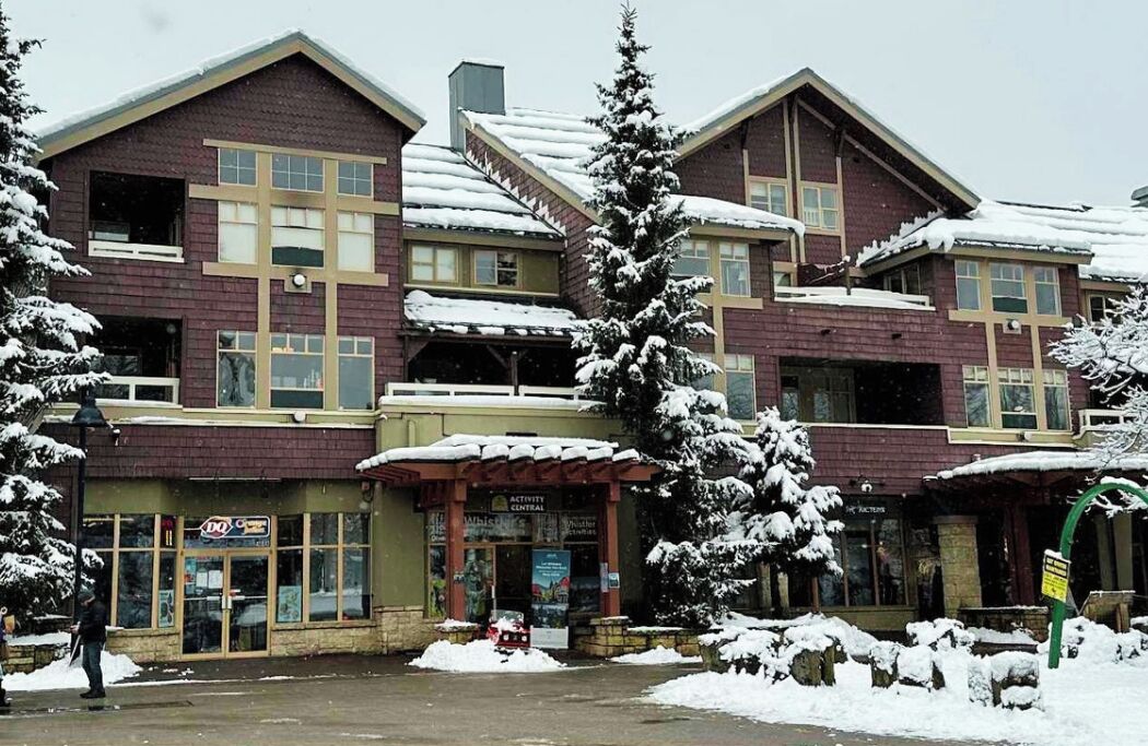 A multi-story building with a central entrance, snow-covered trees, and a visible sign for a business.