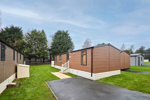 A row of mobile homes with a paved walkway and a grassy area. - Host Stay Serenity Lodge (York)