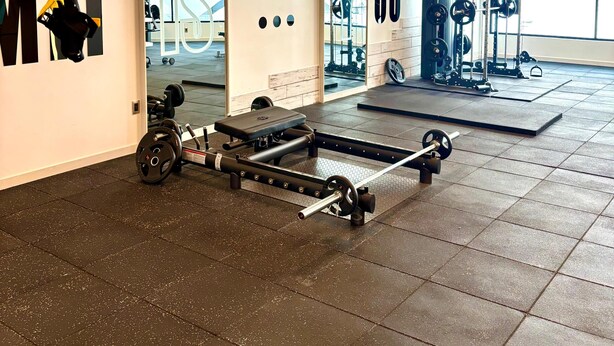 Un gimnasio con equipo de levantamiento de pesas, una prensa de banca y una estructura para sentadillas.