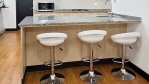 Una cocina moderna con encimera de granito, tres taburetes blancos y armarios de madera.