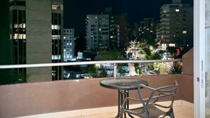 Un balcón con mesa y sillas, con vistas a un paisaje urbano nocturno.