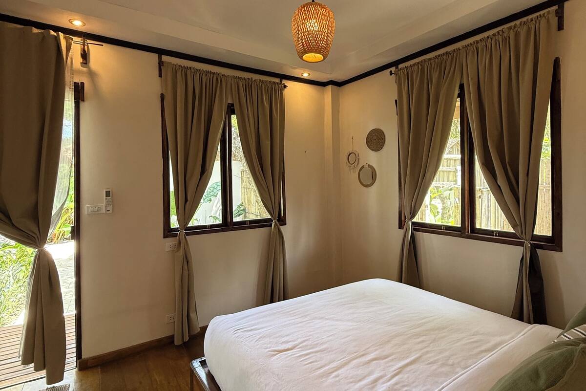 A bedroom with a large bed, wooden floor, and curtains on the windows.