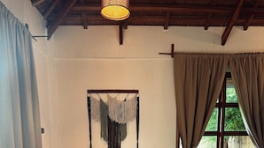 A cozy room with a wooden ceiling, a bed, a sofa with cushions, a hanging macrame decoration, and a window with curtains. - Baia beachfront boutique lodge (San Vicente)