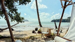 A beachside hammock setup with a view of the ocean, a thatched roof structure, and a sandy beach. - Baia beachfront boutique lodge (San Vicente)