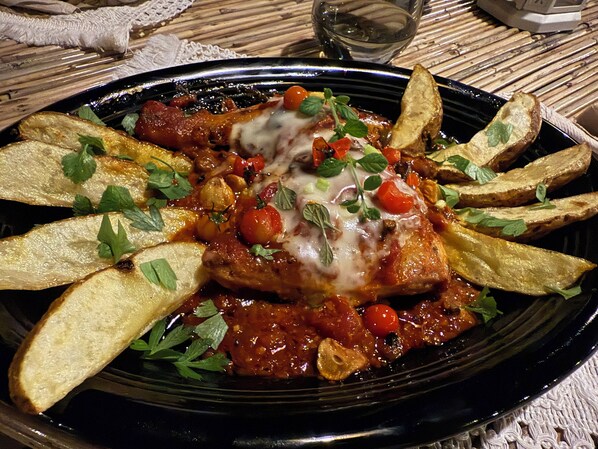 A plate of food with a black rim, containing a main dish with a red sauce, garnished with herbs, and surrounded by golden-brown potato wedges. - Baia beachfront boutique lodge (San Vicente)