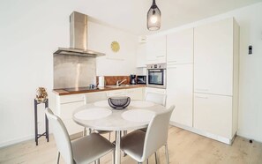 Une cuisine moderne avec des meubles blancs, une table de salle à manger ronde et un luminaire suspendu.