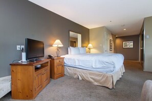 A hotel room with a bed, a TV on a wooden stand, two bedside lamps, a mirror, and a carpeted floor. - Whistler Family Central | Full Kitchen & Balcony | Walk to Parks & Lifts (Whistler)