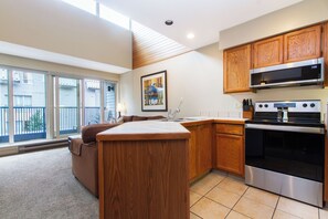 A modern kitchen with wooden cabinets, a stainless steel oven, and a large window overlooking a balcony. - Whistler Village Stay | Spacious Comfort w/Full Kitchen & Fireplace | Ski Access (Whistler)