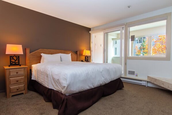 Een slaapkamer met een groot bed, twee bedlampjes, een nachtkastje en een raam met uitzicht op bomen.