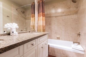 Een badkamer met een bad, een douche, een wastafel met spiegel en een handdoekrek.
