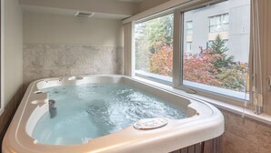 Un jacuzzi con panel de control, una ventana que ofrece vistas a árboles y edificios, y una pared de azulejos.