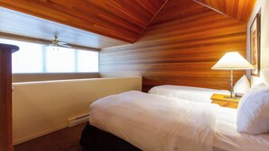 Un dormitorio con dos camas, techo de madera, una ventana y una mesita de noche con lámpara.
