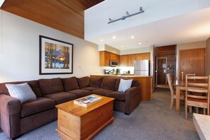 Ein modernes Wohnzimmer mit einem braunen Ecksofa, einem Holztisch und einem gerahmten Gemälde an der Wand.