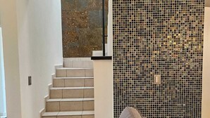 Un saló modern amb un sofà gris, un coixí vermell i una paret de mosaic.
