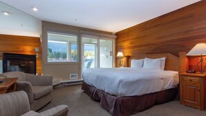 Ett modernt hotellrum med en stor säng, en sittgrupp med soffa och fåtölj, en öppen spis och utsikt över omgivningarna genom stora fönster.