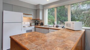 A modern kitchen with grey cabinets, a large island with brown tiles, a white refrigerator, and a microwave. - Whistler Escape w/ Slope Access | Walk to Lifts & Village Fun | Near Gondola (Whistler)