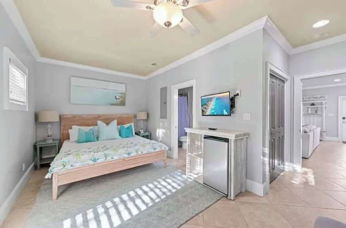 Un dormitorio con cama, televisión, ventilador de techo y una pequeña kitchenette.