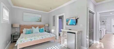 Un dormitorio con cama, televisión, ventilador de techo y una pequeña kitchenette.
