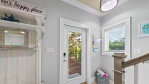 A hallway with a white door, a blue mat, a basket, and a sign that reads "our happy place". - Blu’s Away - Short Walk to the Beach! Just steps from the Pool! Rooftop Deck with beautiful views! Sleeps 12 (Santa Rosa Beach)