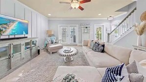 A spacious living room with a large flat-screen TV, a ceiling fan, and a staircase leading to another level. - Blu’s Away - Short Walk to the Beach! Just steps from the Pool! Rooftop Deck with beautiful views! Sleeps 12 (Santa Rosa Beach)