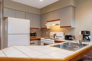 A compact kitchen with a refrigerator, microwave, stove, sink, and a coffee maker. - Whistler Village Lofted Suite | Mountain Views + Best Location (Whistler)