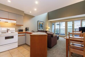 A compact kitchen with a stove, toaster, and coffee maker, a dark-colored sofa, and a wooden dining table with chairs. - Whistler Village Lofted Suite | Mountain Views + Best Location (Whistler)