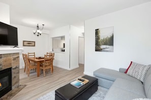 Een moderne woonkamer met een grijze bank, een houten eettafel en een open haard.
