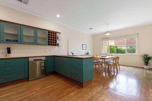 A modern kitchen with teal cabinets, a stainless steel dishwasher, and a dining area with a wooden table and chairs.
