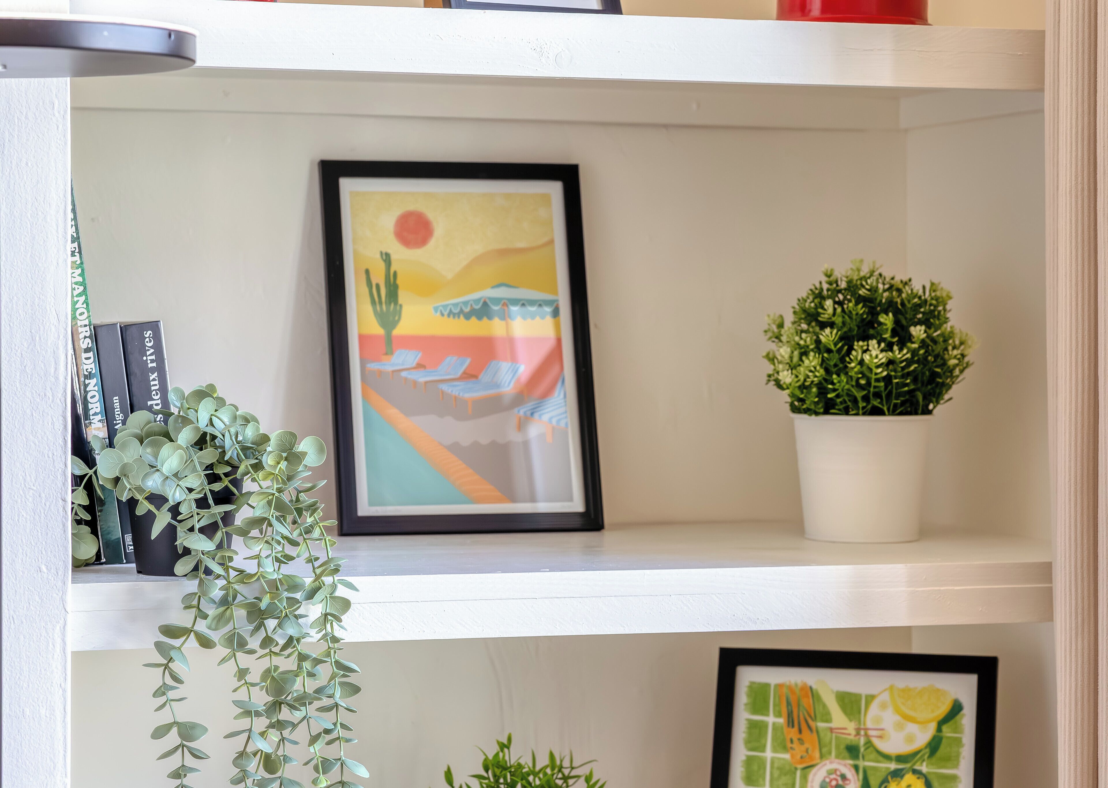 A shelf with a framed painting, a potted plant, and books.