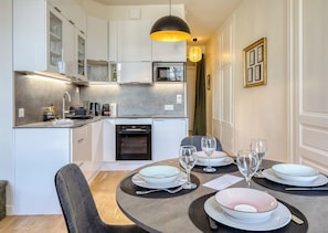 A modern kitchen with white cabinets, a built-in oven, and a dining area set for four with plates and glasses. - Manon, magnifique F2 avec vue (Rouen)