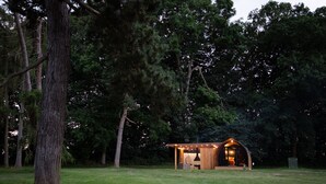 Een houten hutje met een veranda, omringd door bomen en een gazon.