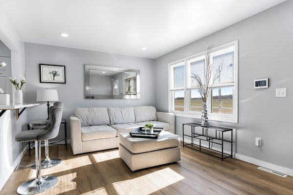 A modern living room with a sofa, a coffee table, a chair, and a large window.