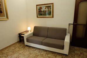 A room with a sofa, a small table with a lamp, a framed picture on the wall, and a door. - Casa Ariel - Cozy Apartment with Terrace in the Heart of Monteverde (Roma)