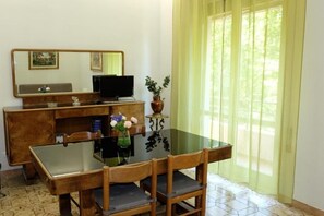 A room with a wooden desk, a computer, a glass table, and chairs. There is a window with curtains. - Casa Ariel - Cozy Apartment with Terrace in the Heart of Monteverde (Roma)