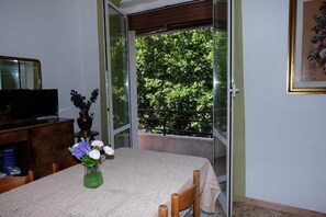 A room with a table, a chair, a television, a vase with flowers, and a window with a view of trees. - Casa Ariel - Cozy Apartment with Terrace in the Heart of Monteverde (Roma)