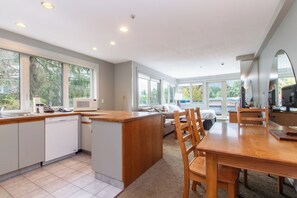 A modern kitchen with a central island, large windows, and a dining area with wooden furniture. - Whistler Family Central | Full Kitchen & Balcony | Walk to Parks & Lifts (Whistler)