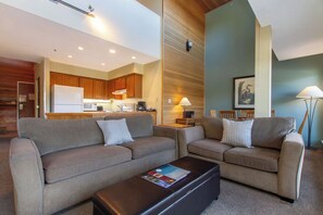 A modern living room with two sofas, a coffee table, and a kitchen in the background. - Whistler Family Central | Full Kitchen & Balcony | Walk to Parks & Lifts (Whistler)