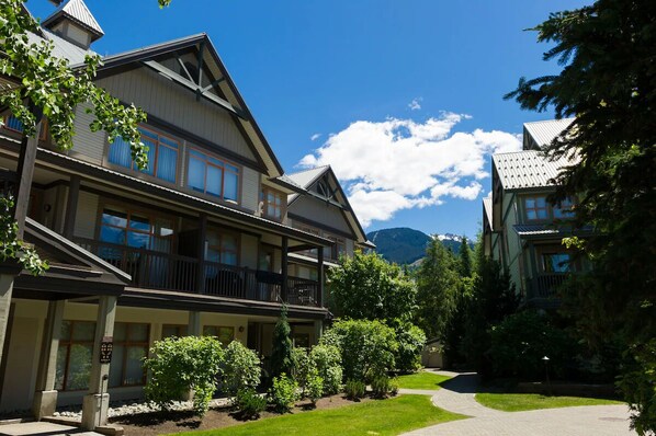 A two-story building with a balcony, surrounded by greenery and a mountain in the background.