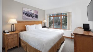Habitación de hotel con una cama grande, dos mesitas de noche con lámparas, un escritorio con computadora, televisión y ventana con vista a árboles y montañas.