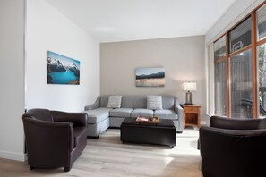 Una sala de estar moderna con un sofá seccional, un reposapiés negro y dos sillones. Hay dos cuadros colgados en la pared que representan paisajes.