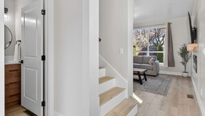 Un interior modern amb una escala que condueix a una zona d'estar, un sofà i una finestra amb vista a arbres.
