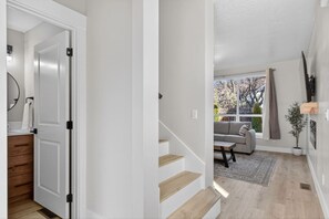 Een modern interieur met een trap die leidt naar een woonruimte, een bank en een raam met uitzicht op bomen.